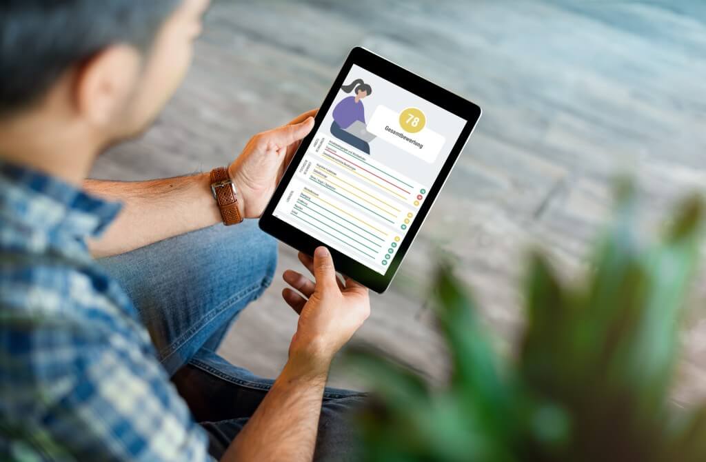 Eine Person hält ein Tablet mit einer Benutzeroberfläche, die Daten und eine Gesamtbewertung anzeigt.