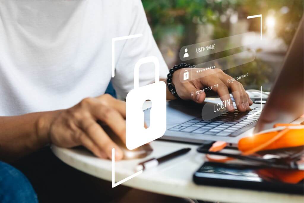 Eine Person tippt an einem Laptop, darüberliegend ein transparentes Schloss und ein Login-Feld.